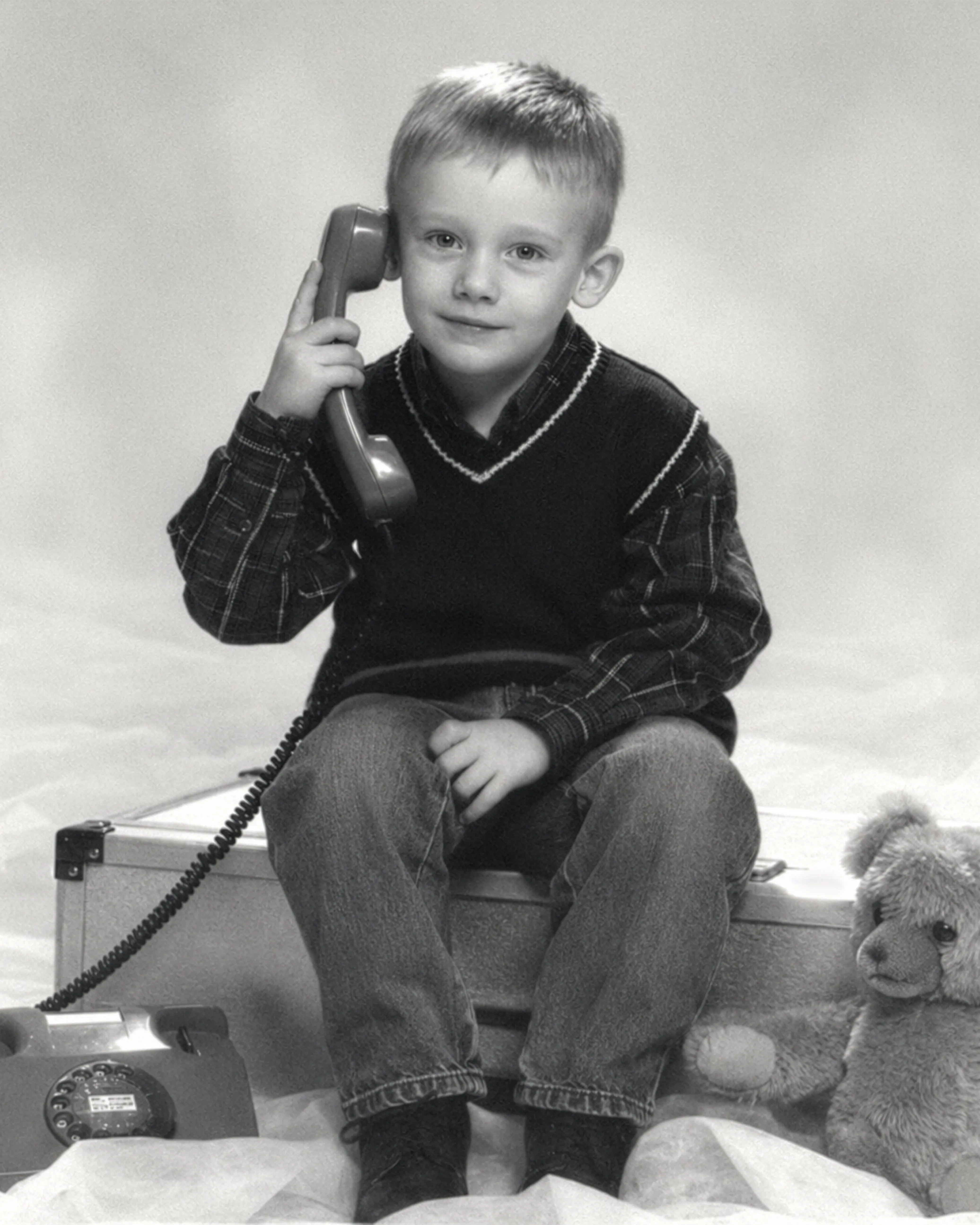 Valentin Lenzing as a child in a black-and-white studio portrait, holding the handset of a rotary phone to his ear, a teddy bear sitting beside him.